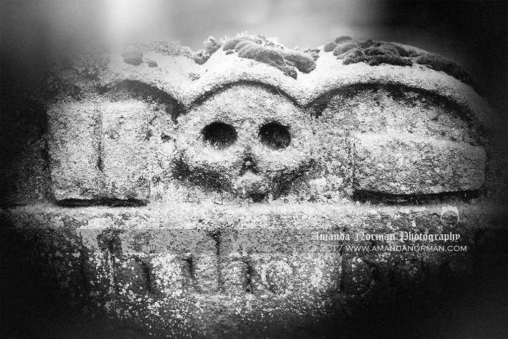 A photograph of a memento mori headstone featuring a skull, book and a coffin